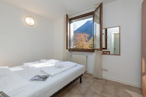 A hotel room with a bed, a window with a view of a mountain, a mirror, and a light fixture. - Porto Letizia Rossini 8, Porlezza, Italy (Porlezza)