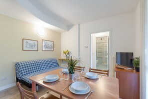 A dining area with a wooden table set for four, a blue sofa, and a television on a stand. - Porto Letizia Rossini 8, Porlezza, Italy (Porlezza)