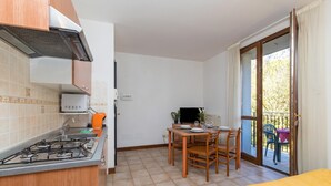 A compact kitchen with a gas stove, a sink, and a small refrigerator. There is a dining area with a table and chairs, and a sliding glass door leading to an outdoor balcony. - Porto Letizia Rossini 7, Porlezza, Italy (Porlezza)