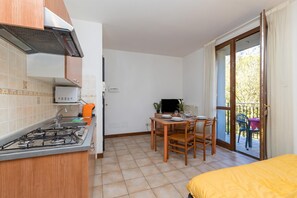 A compact kitchen with a gas stove, a sink, and a small refrigerator. There is a dining area with a table and chairs, and a sliding glass door leading to an outdoor balcony.