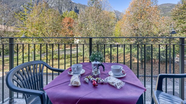A table set with two cups, a teapot, and wrapped chocolates on a balcony with a mountain view.
