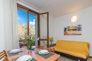 A dining area with a table set for four, a yellow sofa, and a painting on the wall.