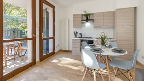 Una cucina moderna con mobili in legno, un'area pranzo con un tavolo apparecchiato per due e vista su un giardino tramite una porta in vetro.