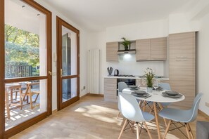 A modern kitchen with wooden cabinets, a dining area with a table set for two, and a view of a garden through a glass door. - Porto Letizia Rossini 4, Porlezza, Italy (Porlezza)