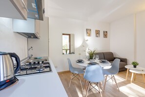 A modern kitchen with a gas stove, a kettle, and a dining area with a table and chairs. - Porto Letizia Rossini 4, Porlezza, Italy (Porlezza)