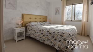 Un dormitorio con cama, mesita de noche, decoración en la pared y ventana con cortinas.