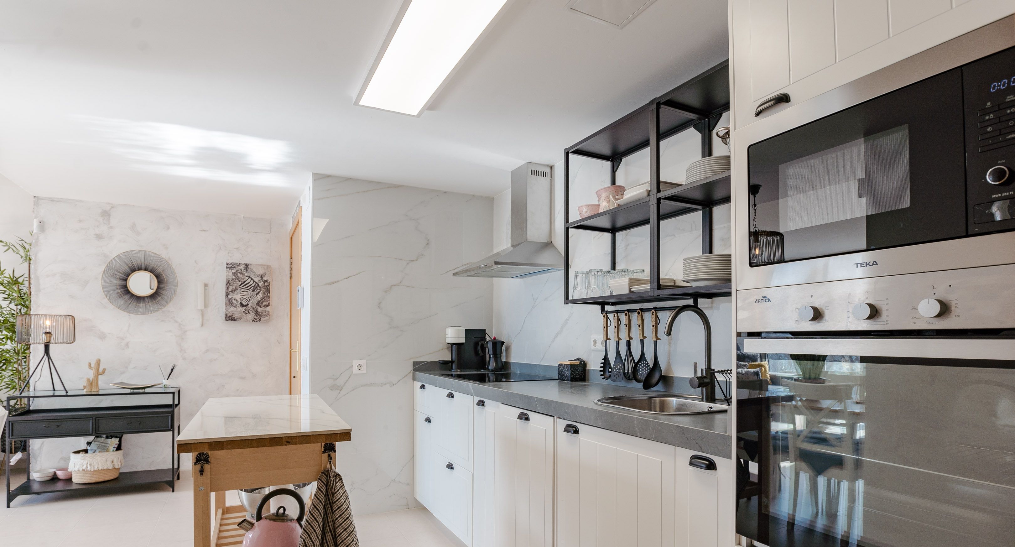 Una cocina moderna con armarios blancos, encimera negra y horno empotrado.