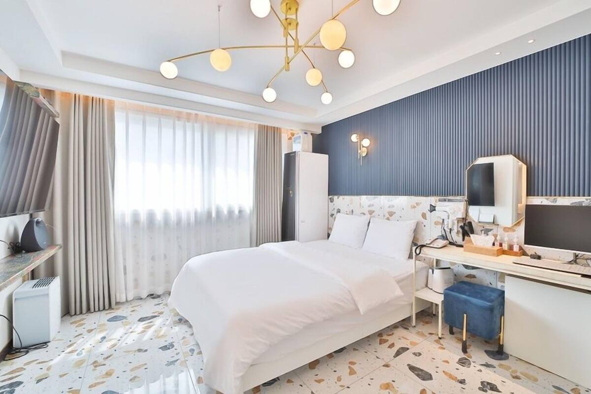 A modern hotel room with a large bed, a desk, a chair, a wardrobe, a mirror, and a television.