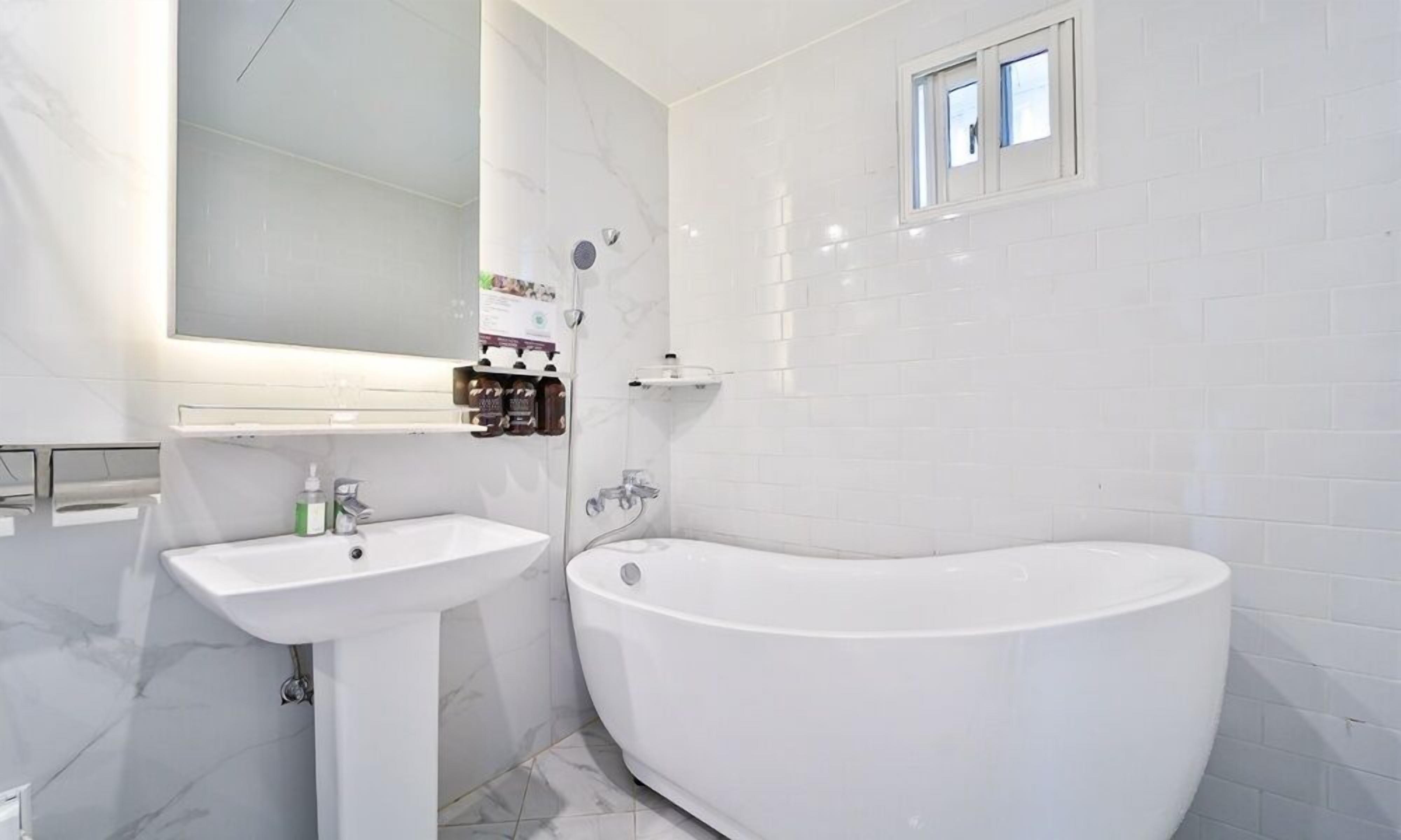 A modern bathroom with a freestanding bathtub, a pedestal sink, and a mirror above the sink.