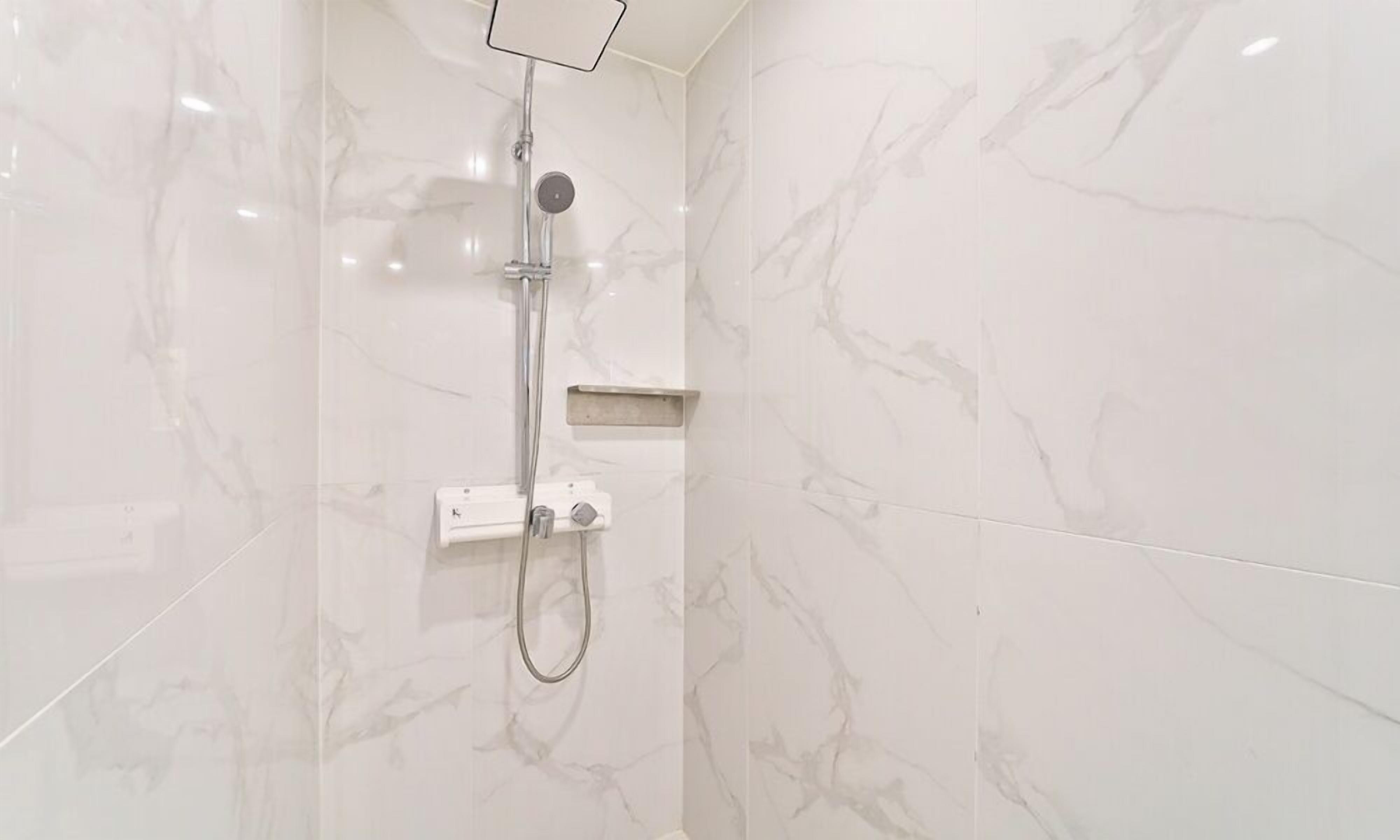 A modern bathroom with a shower, marble walls, and a built-in shelf.