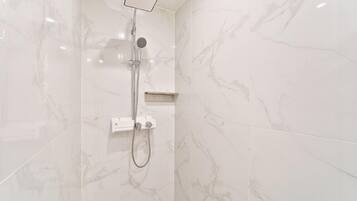 A modern bathroom with a shower, marble walls, and a built-in shelf.