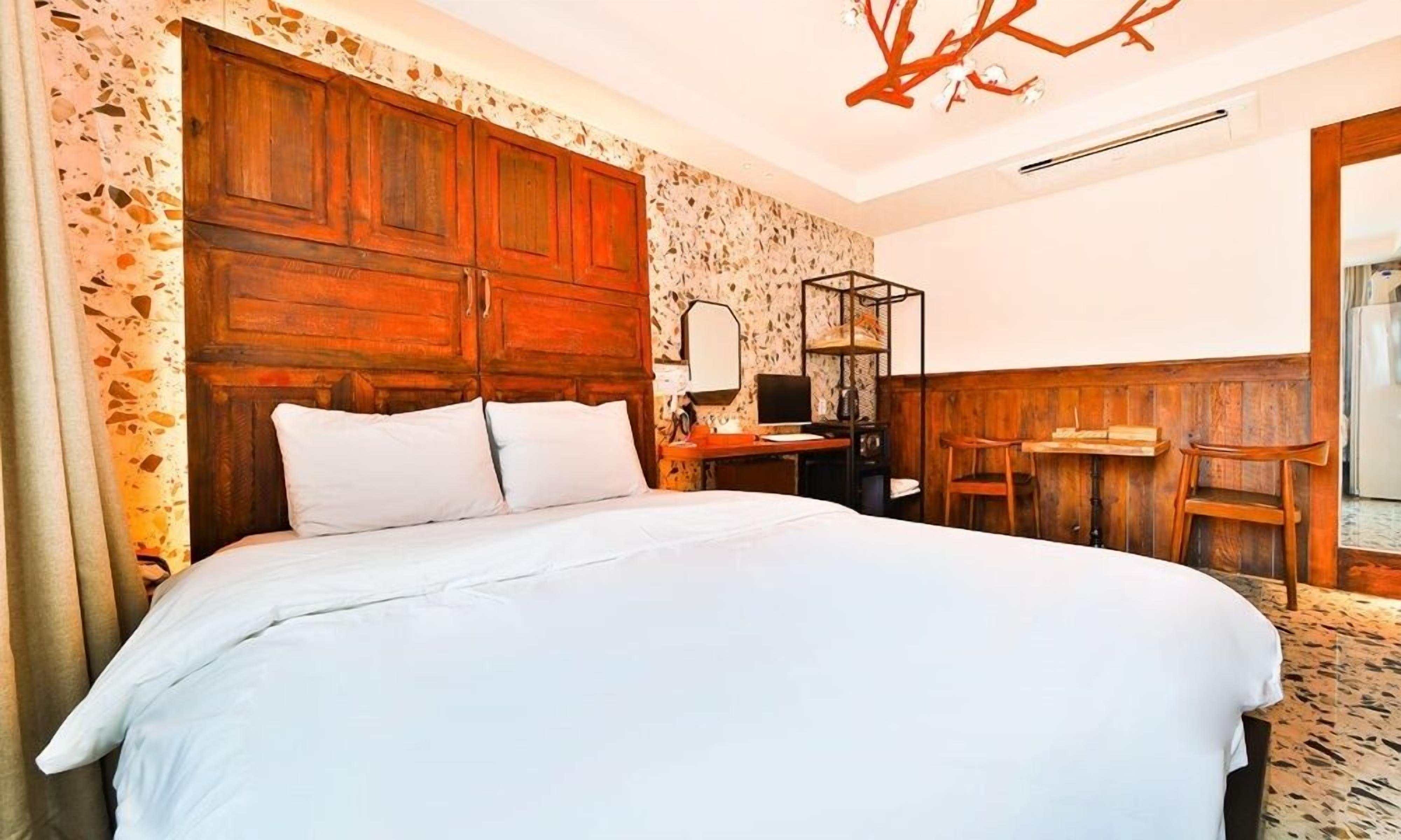A bedroom with a large bed, wooden headboard, a desk with a chair, and a small table.
