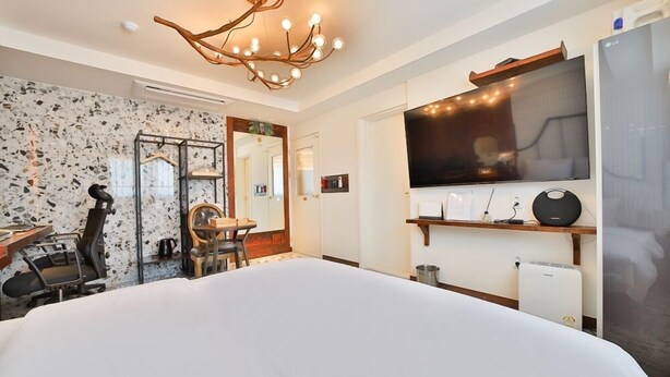 Een hotelkamer met een groot bed, een televisie, een bureau met stoel, een koffieapparaat en een bijzondere kroonluchter.