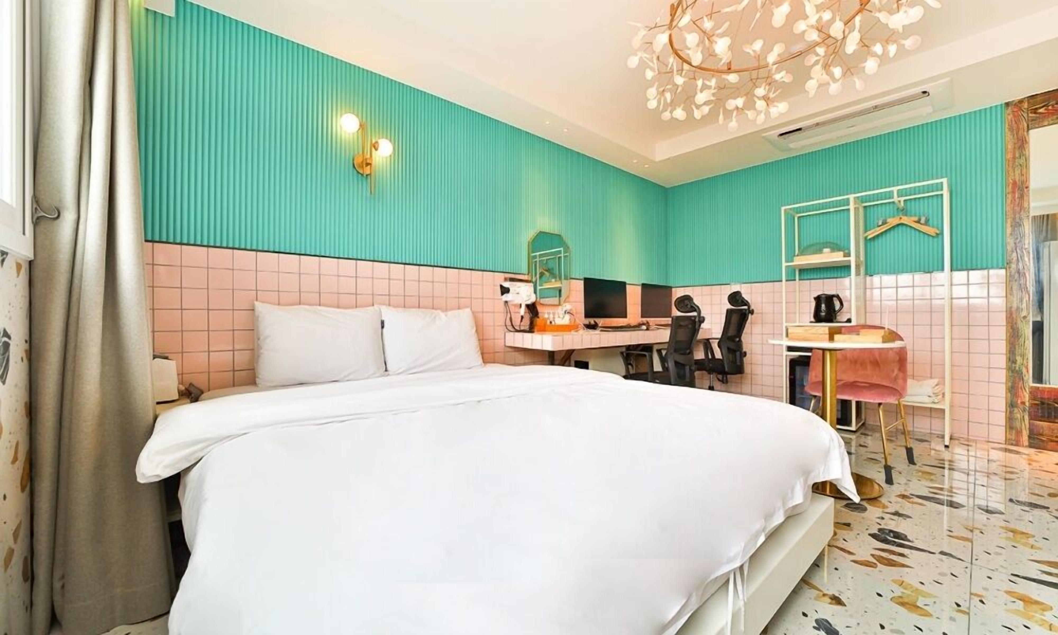 A hotel room with a bed, a desk with a computer, a chair, and a mirror.