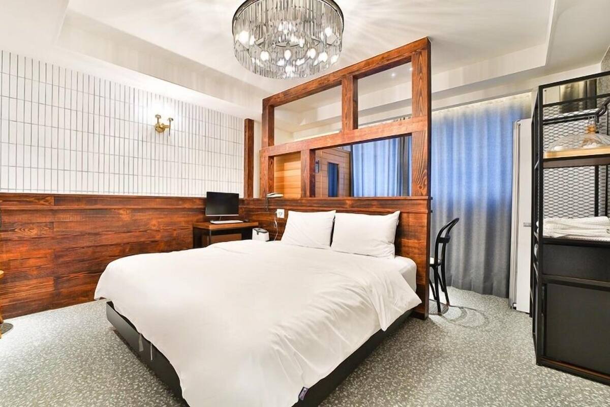 A hotel room with a large bed, wooden headboard, a desk with a chair, a small table, and a mirror.