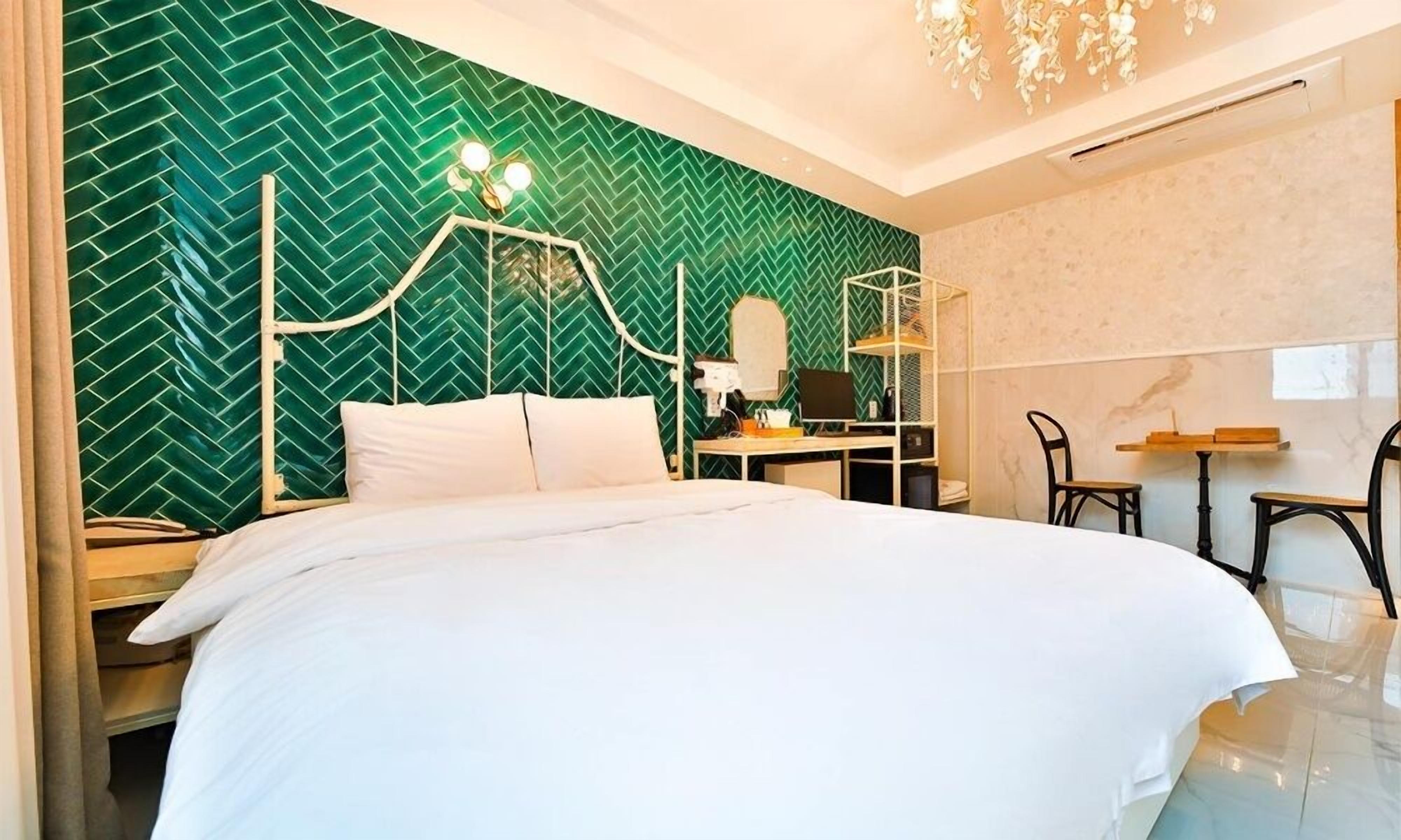 Hotelkamer met een groene muur met een herringbonepatroon, een wit bed, een bureau met een computer en een stoel.