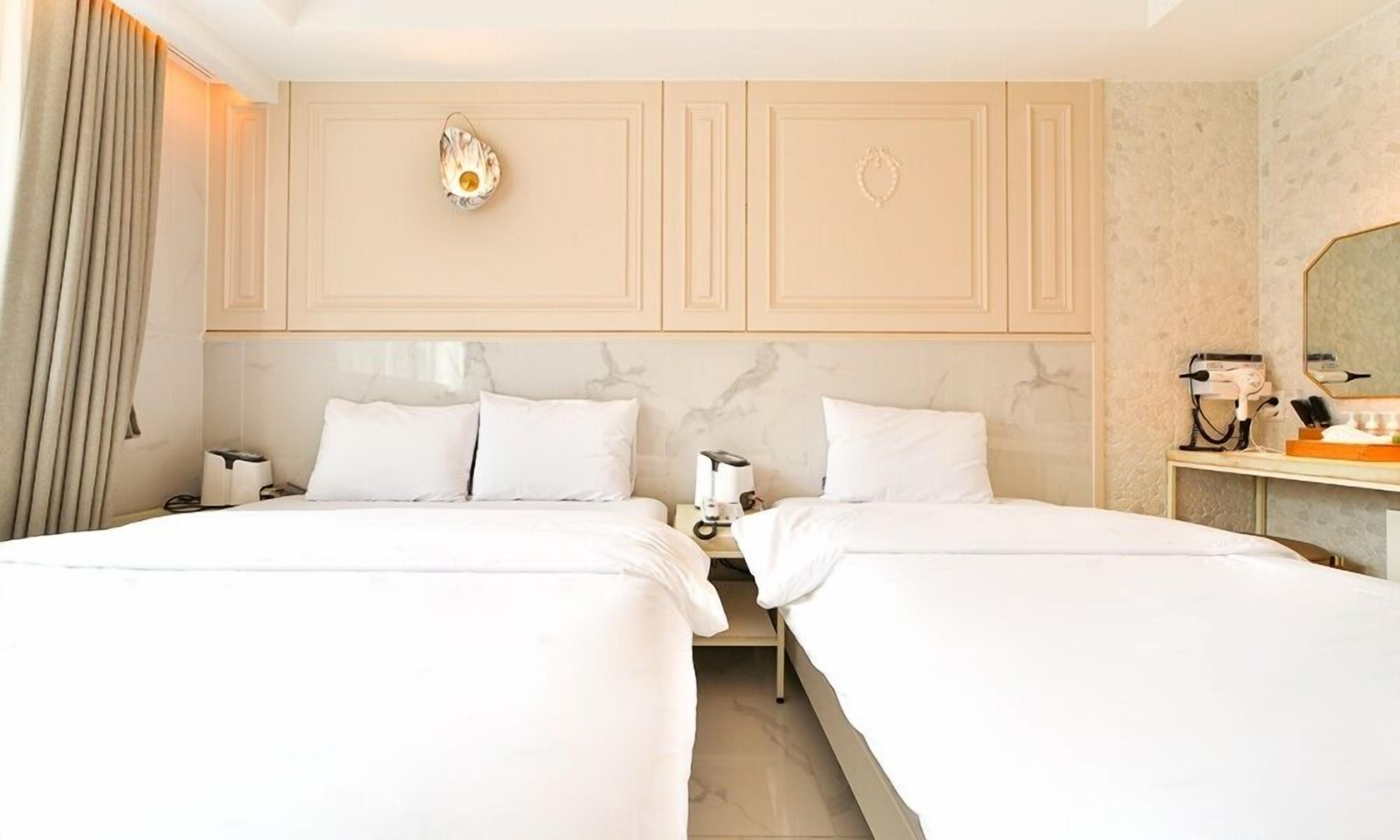 A hotel room with two beds, a nightstand with a lamp, a mirror, and a hairdryer on a table.