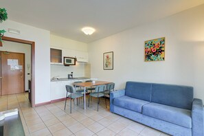 A living room with a blue sofa, a dining table with chairs, a microwave, and a small kitchen area.