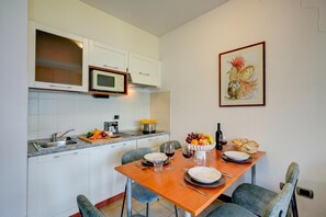 A modern kitchen with white cabinets, a microwave, and a dining table set with plates, glasses, and a fruit bowl.