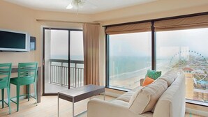 A spacious room with a large window, a sofa, a table, and a TV mounted on the wall. - One Bedroom Condo, Myrtle Beach 3317100 (Myrtle Beach)