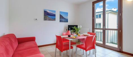 A room with a red sofa, a dining table with red chairs, two wall-mounted pictures, and a large sliding glass door to the outside.