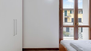 A bedroom with a bed, a wardrobe, and a window with a view of buildings. - Porto Letizia Mascagni 5, Porlezza, Italy (Porlezza)