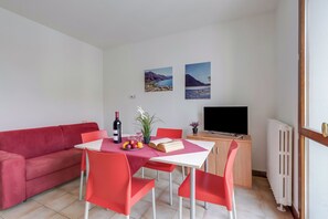 Una sala de estar moderna con un sofá rojo, una mesa de comedor con sillas rojas, un televisor y dos cuadros de paisajes en la pared.
