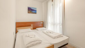 Ein ordentlich bezogenes Bett mit weißen Leinentüchern und Handtüchern, ein hölzerner Kopfseitenverkleidung und ein kleines Landschaftsbild an der Wand.