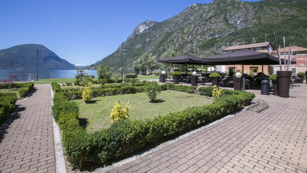 Ein gepflasterter Weg mit einem gepflegten Garten und Sitzbereich im Freien, mit Blick auf ein Gewässer und Berge.