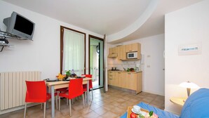 A compact living space with a dining area, kitchenette, and a sofa with a tray of fruit and flowers. - Porto Letizia Venezia 6, Porlezza, Italy (Porlezza)