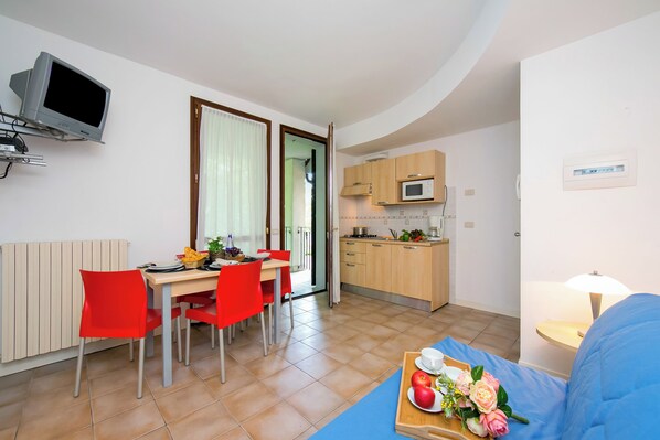Ett kompakt bostadsutrymme med en matplats, ett litet kök och en soffa med ett brickbord som är dekorerat med frukt och blommor.