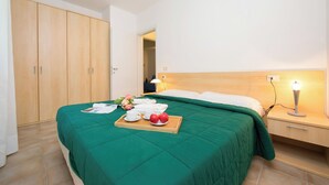 A neatly made bed with a green bedspread, a bedside table with a lamp, and a tray with a cup, apples, and a flower. - Porto Letizia Venezia 6, Porlezza, Italy (Porlezza)