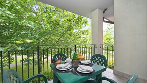 En balkon med et bord dækket til to, med en frugtkurv, en vase med blomster og en kurv med brød.