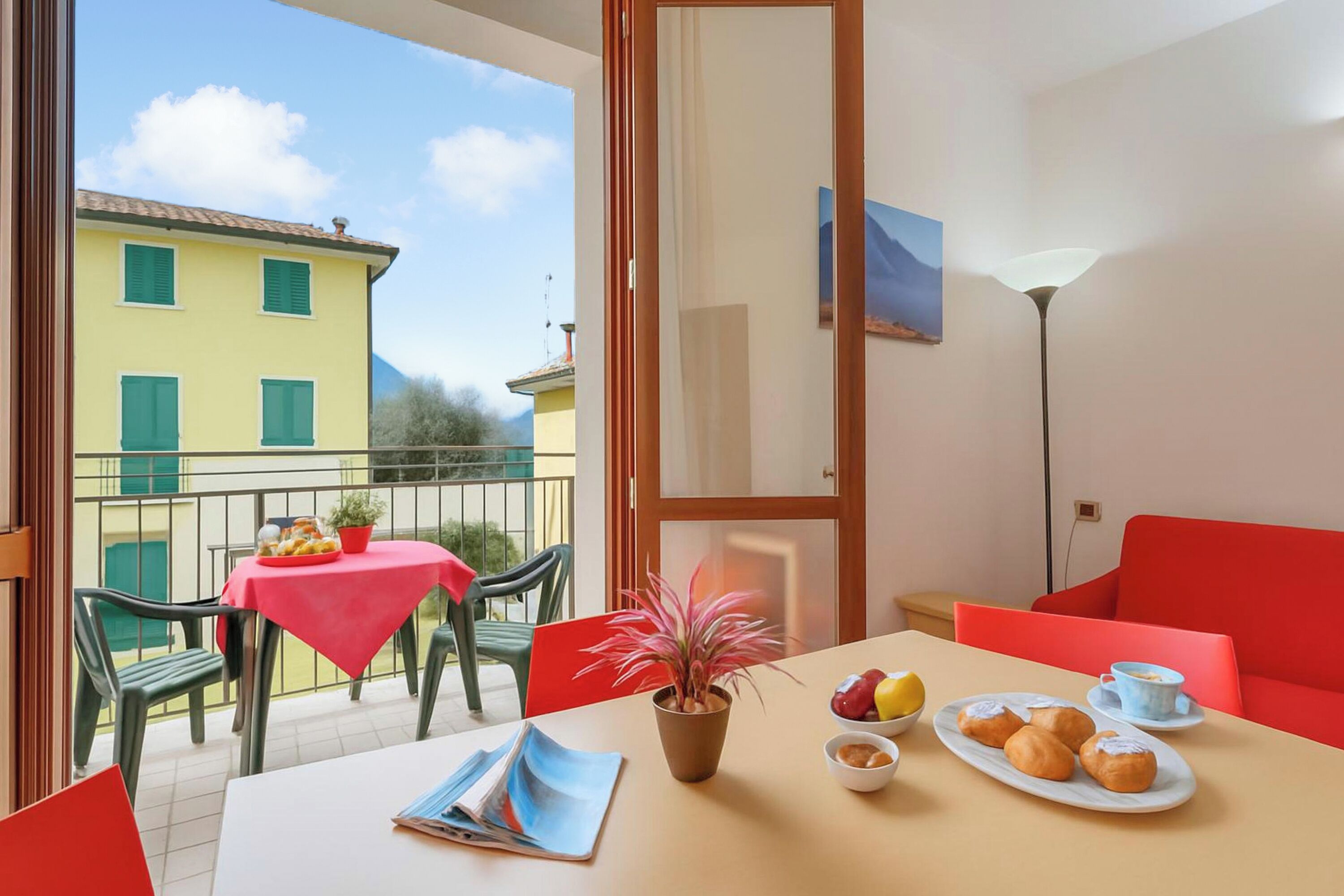 Un balcon avec une table, des chaises, un pot de fleurs et une table où sont disposés de la nourriture et des boissons.