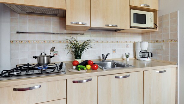 A kitchen with wooden cabinets, a microwave, a gas stove, and a sink. - Porto Letizia Venezia 5, Porlezza, Italy (Porlezza)