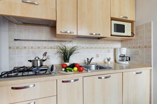 Une cuisine avec des meubles de rangement en bois, un four à micro-ondes, une cuisinière à gaz et un évier.