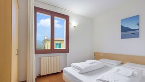 A hotel room with a bed, a window with curtains, a radiator, and a painting on the wall. - Porto Letizia Venezia 5, Porlezza, Italy (Porlezza)