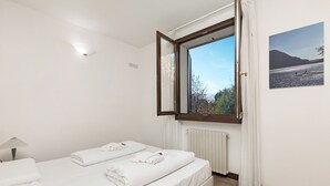Une chambre d’hôtel avec deux lits, une fenêtre donnant sur les montagnes, un radiateur et un tableau accroché au mur.