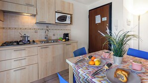 Une cuisine compacte dotée de meubles en bois, d’un four à micro-ondes, d’un évier et d’une table à manger avec des chaises.