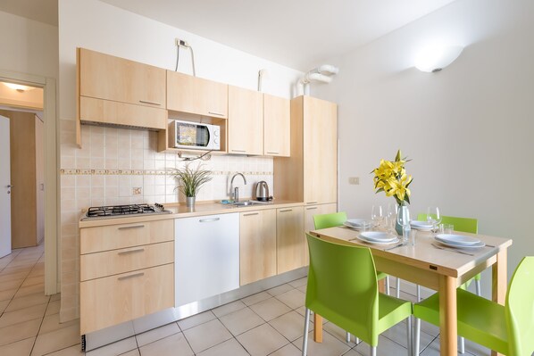 A modern kitchen with wooden cabinets, a microwave, and a dining table set for two with green chairs. - Porto Letizia Mascagni 6, Porlezza, Italy (Porlezza)