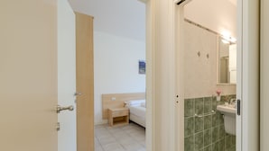 A hotel room with a bed, bedside table, and a bathroom with a sink and mirror.