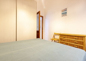 Una camera da letto con un letto, una cassettiera in legno, una sedia e una porta che dà su un'altra stanza.