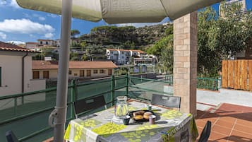 A terrace with a table set for two, a green mesh fence, and a view of buildings and trees in the background.