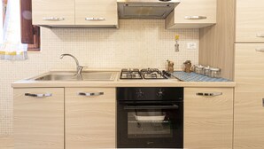 A kitchen with a sink, stove, oven, and wooden cabinets. - Atena holiday apartment in Seccheto few steps away from the beach (Campo nell'Elba)