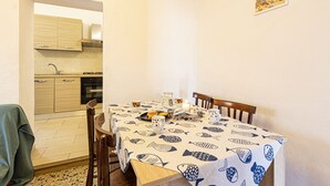 A dining area with a table set for two, a kitchen in the background, and a framed picture on the wall. - Atena holiday apartment in Seccheto few steps away from the beach (Campo nell'Elba)