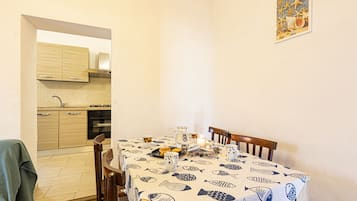 A dining area with a table set for two, a kitchen in the background, and a framed picture on the wall.