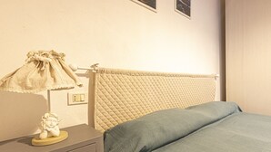 A bedroom with a bed, a nightstand, a lamp, and a wall-mounted outlet. - Atena holiday apartment in Seccheto few steps away from the beach (Campo nell'Elba)