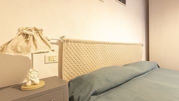 A bedroom with a bed, a nightstand, a lamp, and a wall-mounted outlet.