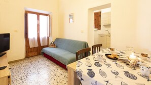 A cozy living room with a sofa, a dining table with a fish-patterned tablecloth, and a kitchen visible through an archway. - Atena holiday apartment in Seccheto few steps away from the beach (Campo nell'Elba)