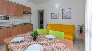 Une cuisine compacte avec des meubles en bois, un four à micro-ondes et un évier. On y trouve une table à manger recouverte d’une nappe colorée et agrémentée d’une plante en pot.